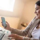 Kobieta z telefonem w dłoni, pracująca przy laptopie. Czy to koincydencja, że oboje patrzą na morze?