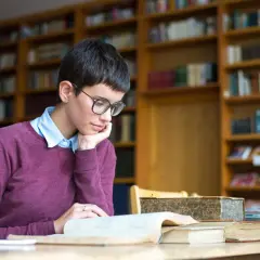 Młoda kobieta w okularach pochłonięta lekturą, szukająca odpowiedzi na pytanie: transcendencja co to? W otoczeniu bibliotecznych regałów.