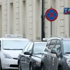 Kurier z pomarańczową torbą Pyszne.pl mija rząd samochodów taxi. Na ulicy widać znaki zakazu postoju.