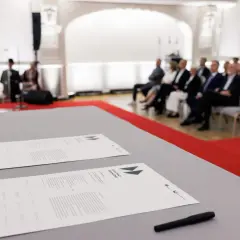 Na stole leżą dokumenty z napisem "SZLAK PRACY ORGANICZNEJ". W tle siedzą ludzie, czekając na rozpoczęcie wydarzenia, które symbolizuje pracę u podstaw.