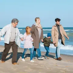 Rodzina spaceruje po plaży. Dziadkowie, ich córka, zięć i dwójka wnuków trzymają się za ręce.