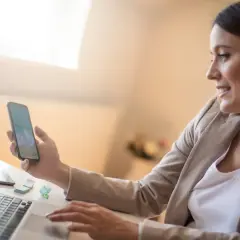 Kobieta z telefonem w dłoni, pracująca przy laptopie. Czy to koincydencja, że oboje patrzą na morze?