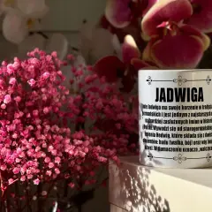 Biały kubek z napisem "Jadwiga" i opisem znaczenia imienia, na tle różowych kwiatów i storczyków.