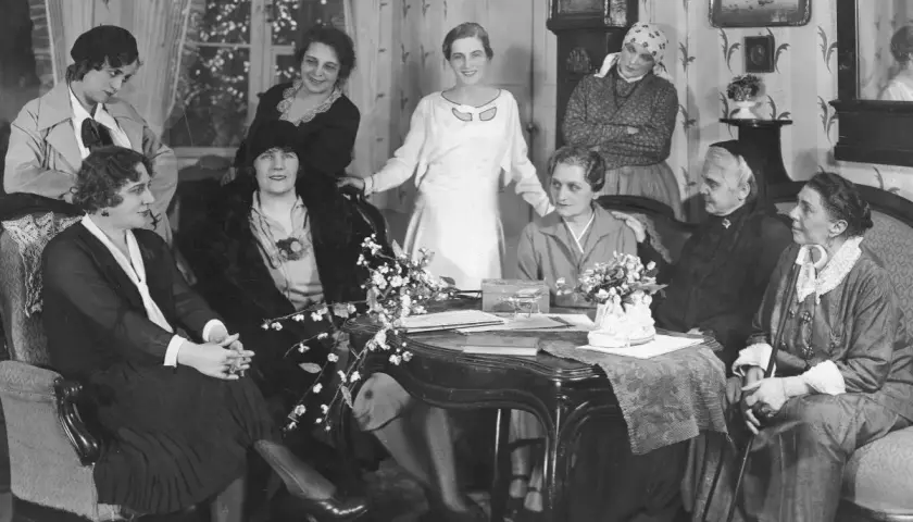 Grupa kobiet w eleganckich strojach, symbol emancypacji kobiet w lalce, dyskutuje przy stole.