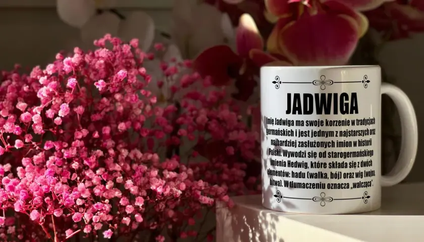 Biały kubek z napisem "Jadwiga" i opisem znaczenia imienia, na tle różowych kwiatów i storczyków.