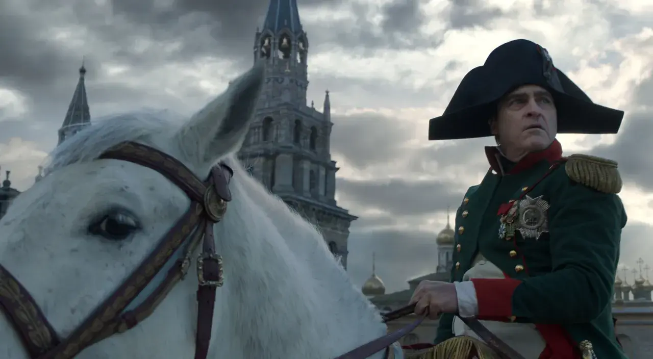 Buńczuczny Napoleon na białym koniu, w tle moskiewskie cerkwie. Jego spojrzenie sugeruje determinację i nieustępliwość.
