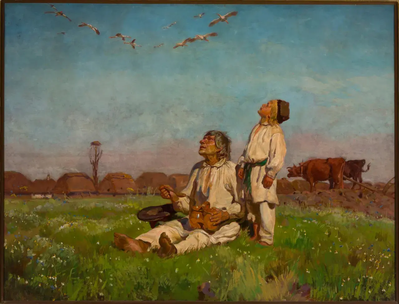 Dwóch mężczyzn w strojach ludowych patrzy na ptaki w locie nad polami i chatami.