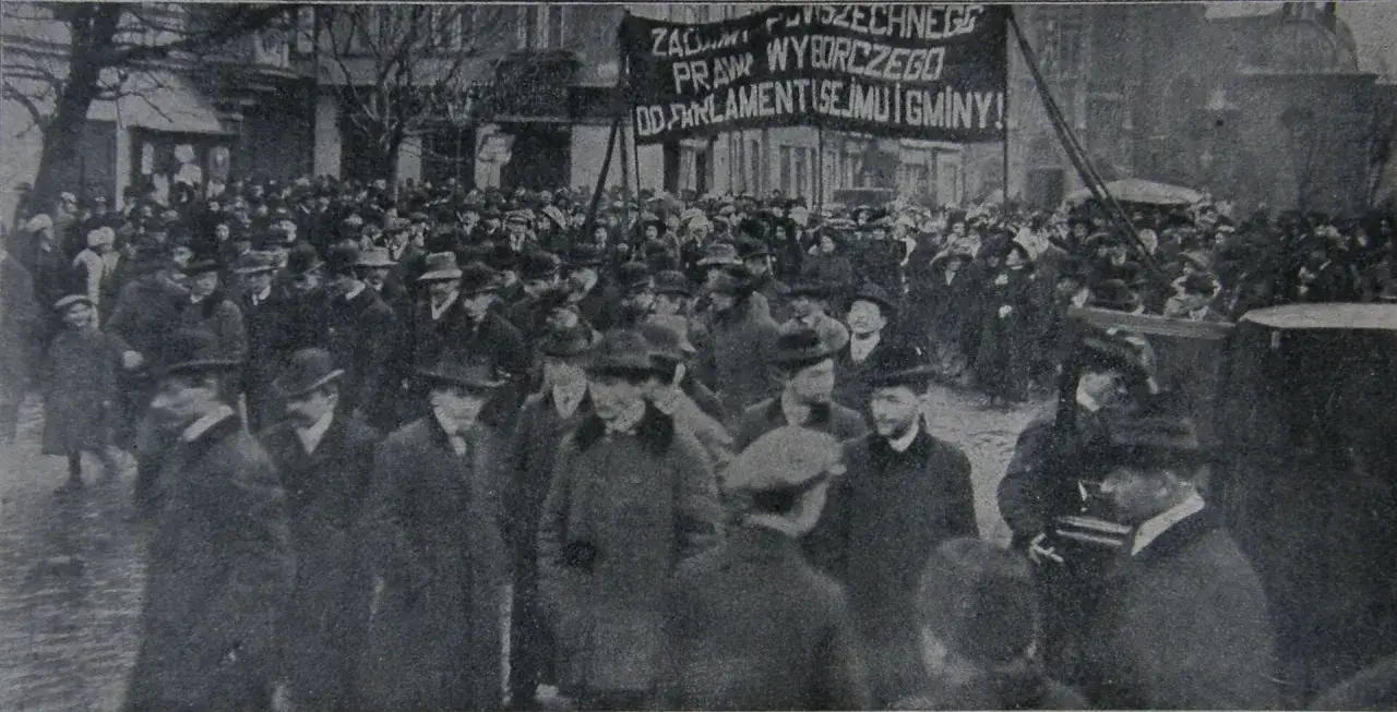 Tłum ludzi na ulicy, z transparentem o prawach wyborczych. To obraz emancypacji kobiet w lalce, symbol walki o równość.
