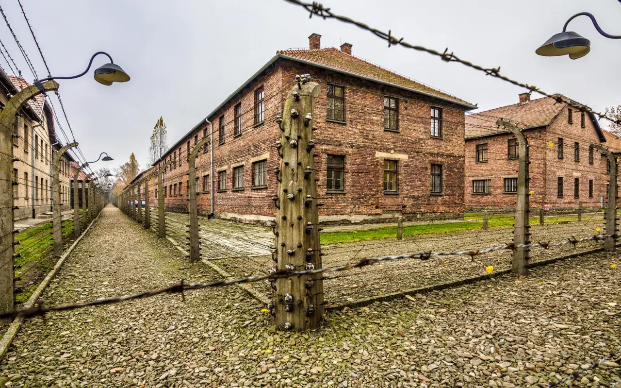 U nas w Auschwitzu streszczenie: ceglane budynki obozu, druty kolczaste i kamienista ścieżka.